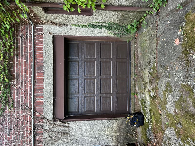Dark brown raised-panel garage door on brick home with ivy in Massachusetts