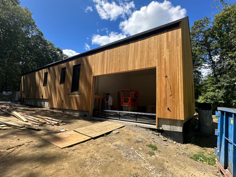 Modern cedar-clad building under construction with large garage opening — MA project